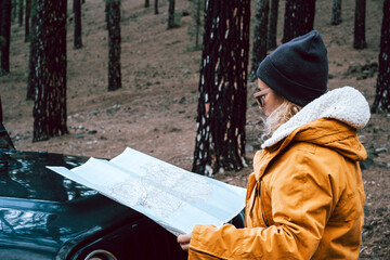 Woman check paper map in the woods forest on the front of the black off road car - concept of...
