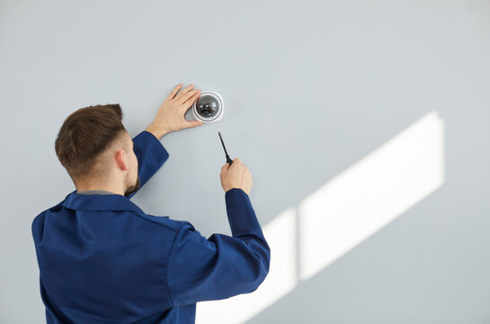 Male technician installing surveillance camera on light copy space wall. Back view of repair service worker using screwdriver to fit screws and adjust wall mounted CCTV security dome cam inside house