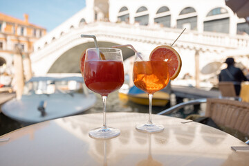 Two summer alcohol coctails on the table at outdoor cafe near Grand Canal and Rialto ridge in Venice. Italian Spritz Aperol drink at famous landmark in Italy