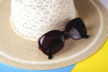 Sunglasses lie on the brim of a wicker hat.