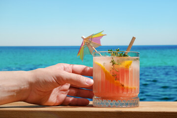 Hand holds glass of hard seltzer summer cocktail at beach bar.