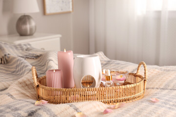 Fototapeta na wymiar Aroma lamp, bottle of oil and burning candles on wicker tray in bedroom