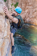 Young male climber strong success hiking on rocks over the sea with rope and helmet.