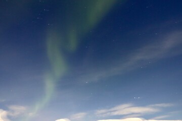 northern lights in norway near tromso. green lights and blue sky with clouds.