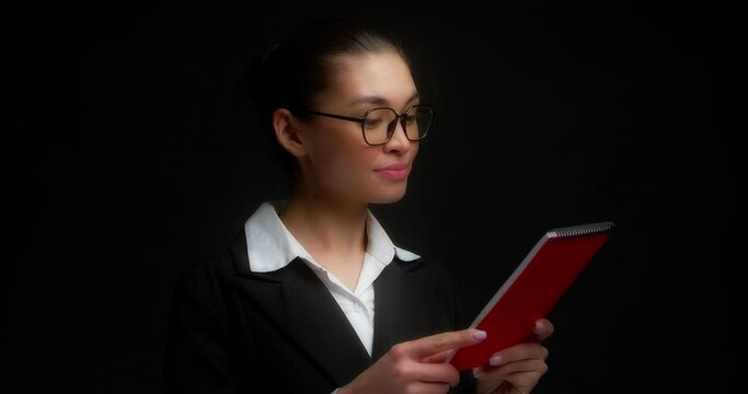 The Female Boss Is Handed A Red Notebook From Behind The Scenes. A Business Woman Listens To The Manager And Gives A Thumbs Up. Isolated On A Black Background