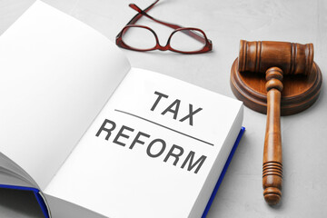 Book with text TAX REFORM, gavel and glasses on light grey table