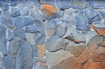 Granite - rock stone wall texture. Exterior wall of decorative broken stone in blue -grey- orange colors. Building industry concept