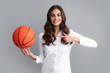 Happy woman pointing finger on basketball ball, isolated on gray background.