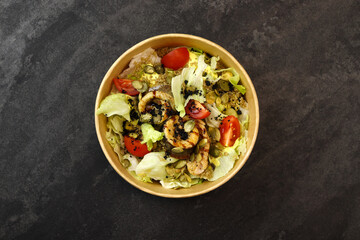 Salad with fish. Fresh vegetable salad with baked fish fillet. Fish salad with fried fillet and fresh vegetables in eco paper bowl on dark background. Food delivery service and daily ration concept.