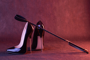 Black shiny high heel shoes and a whip on a dark background