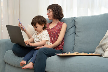 Mother and her daughter sitting on a sofa using a mobil phone and a laptop. Addiction to computers, phones, gadgets, bad habit. 