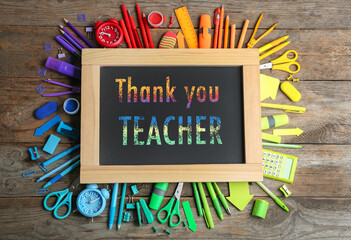 Small blackboard with phrase Thank You Teacher and different colorful stationery on wooden table,...