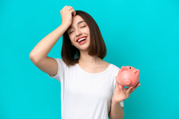 Young Ukrainian woman holding a piggybank isolated on blue background has realized something and intending the solution