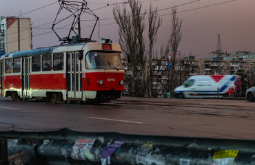 Naklejka na ściany i meble A red tram runs in the middle of the road. Public transport. The tram goes in cloudy weather