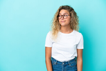 Girl with curly hair isolated on blue background making doubts gesture looking side