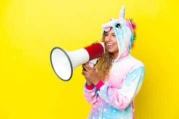 Girl with curly hair wearing a unicorn pajama isolated on yellow background shouting through a...
