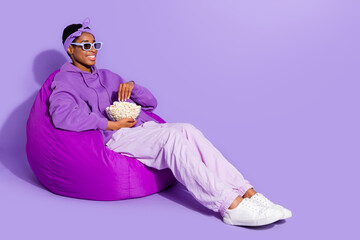 Photo of relaxed transgender sit bean bag watch movie eat popcorn wear headband hoodie isolated purple color background