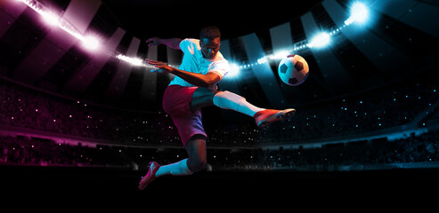 Professional football or soccer player in action on stadium with flashlights, kicking ball for...