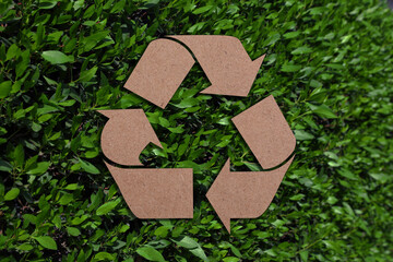 Recycling symbol cut out of kraft paper and fresh green leaves on background