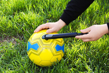 Man inflating soccer ball with manual pump on green grass, closeup