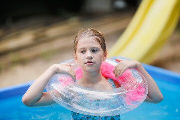 European preteen girl in swimsuit swims on circle in pool in backyard. Funny child with an...