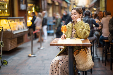 Woman sitting with a cocktail at outdoor bar or restaurant on the crowded street in Bologna....