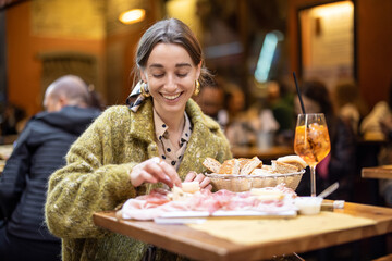 Woman eating italian meat appetizer, various sliced meat and cheese with bread and Aperol Spritz at bar or restaurant outdoors. Concept of Italian lifestyle and gastronomy