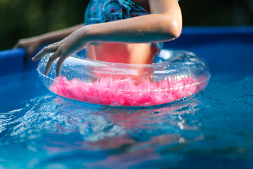 European preteen girl in a swimsuit swims on a circle in the pool in the backyard. rubber ring with...