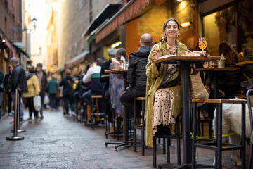 Woman sitting on crowded street at bar or restaurant outdoors in Bologna city. Concept of Italian...