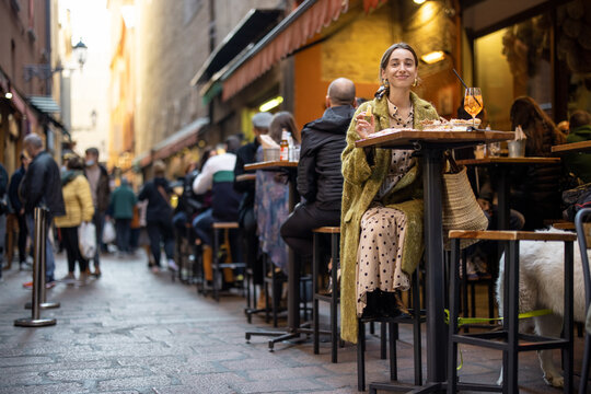 Woman sitting on crowded street at bar or restaurant outdoors in Bologna city. Concept of Italian lifestyle and gastronomy