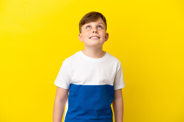 Little redhead boy isolated on yellow background thinking an idea while looking up