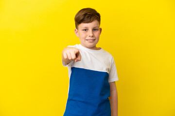 Little redhead boy isolated on yellow background surprised and pointing front