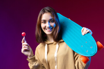 Young beautiful fashionable hipster girl dressed in a hoodie holds a skateboard in her hands on a...