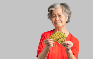 Portrait of a senior woman holding a brain shape made from yellow paper against a gray background