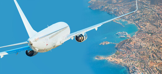 White passenger jet plane in the sky - Aircraft flies high over the city and and sea coast in the...