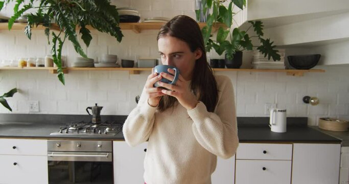 Caucasian non-binary transgender woman drinking coffee in kitchen