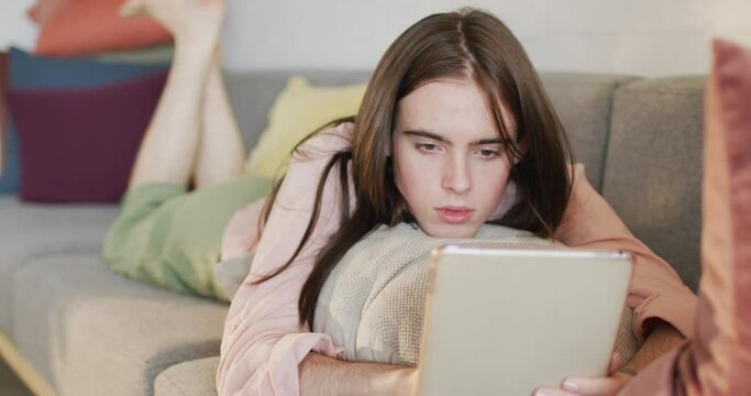 Caucasian non-binary transgender woman lying on sofa, using tablet