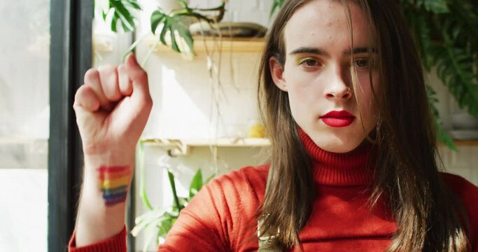 Portrait of caucasian non-binary transgender woman raising hand with lgbt flag