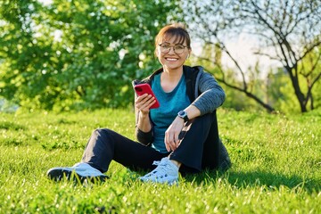 Fototapeta premium Outdoor portrait of mature smiling woman looking at camera sitting on grass