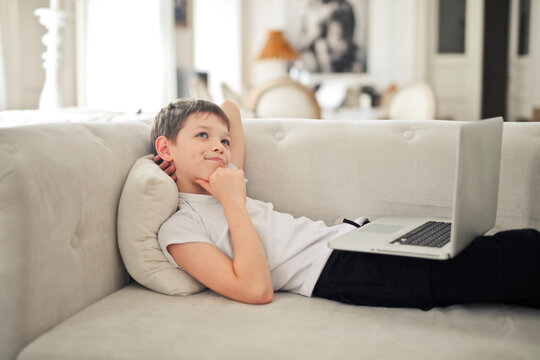 child with a computer in his hand lying on a sofa