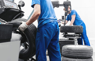 Two mechanics workers balancing wheel in car tire service station on machine