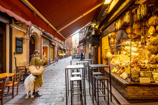 Famous gastronomical street with food stores and restaurants in Bologna city. Woman walking with her dog. Italian food and gastronomy concept