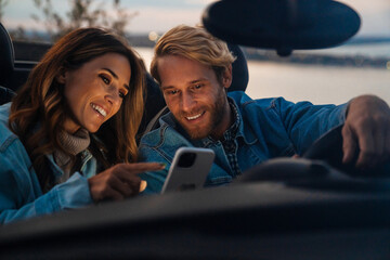 White happy couple smiling and using cellphone during car trip