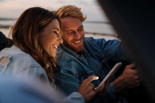 White happy couple smiling and using cellphone during car trip