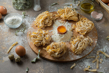 Freshly made tagliatelle pasta with eggs and flour on wooden board