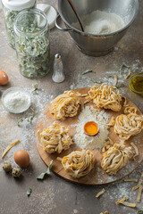 Freshly made tagliatelle pasta with eggs and flour on wooden board