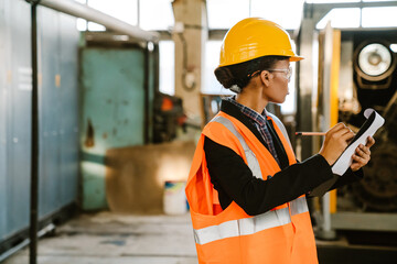 Black woman wearing helmet writing down notes while working at factory