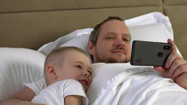 Family watching cartoons. Dad and son with phone in the bedroom