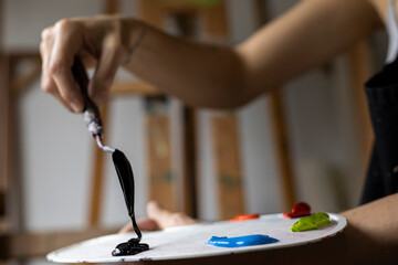 Fototapeta premium Close-up of the hands of an unrecognizable Latin American artist showing the palette and palette knife with the paints she uses to paint in her art studio. Concept of artist and hobby