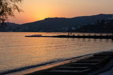 Beautiful orange golden color sunset with Bodrum, Yalikavak silhoutte. With a Aegean Sea and Beach with persons on a hot summer evening.